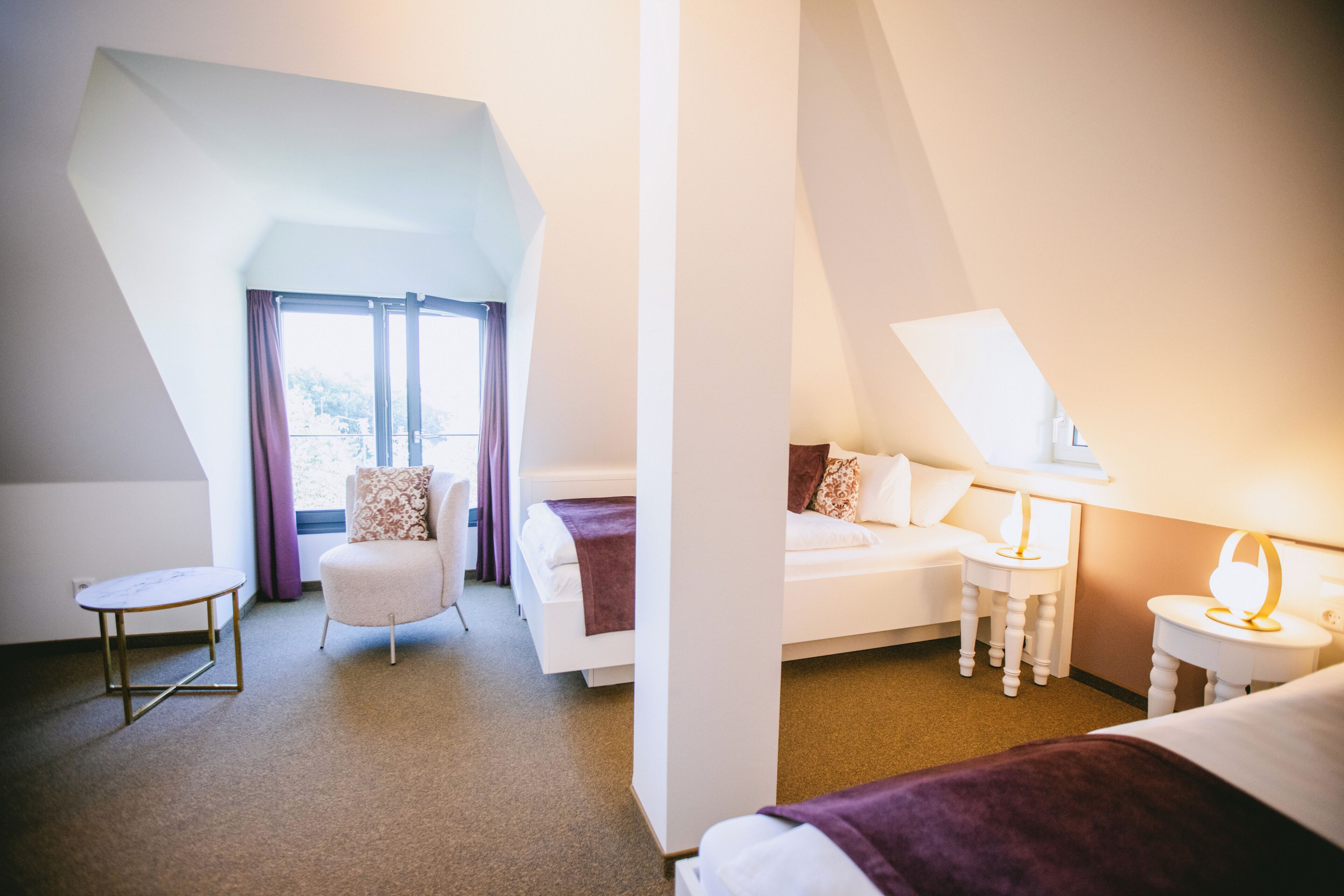 A hotel room with a bed, a chair, a small table, and a lamp.