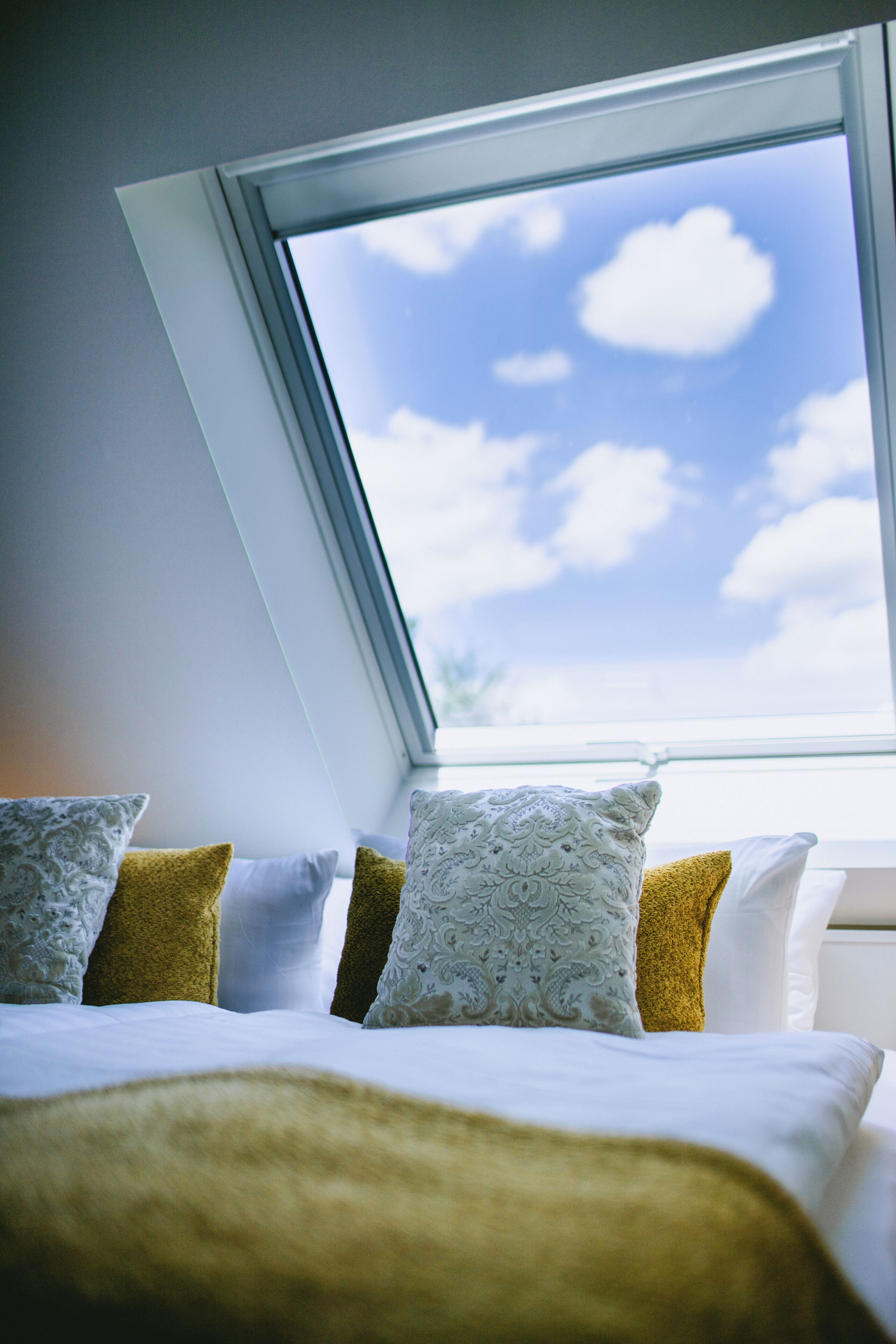 Ein Schlafzimmer mit Dachfenster, einem Bett mit weißer Bettwäsche und dekorativen Kissen.