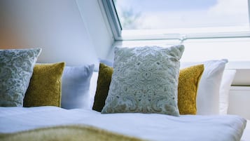 Ein Schlafzimmer mit Dachfenster, einem Bett mit weißer Bettwäsche und dekorativen Kissen.