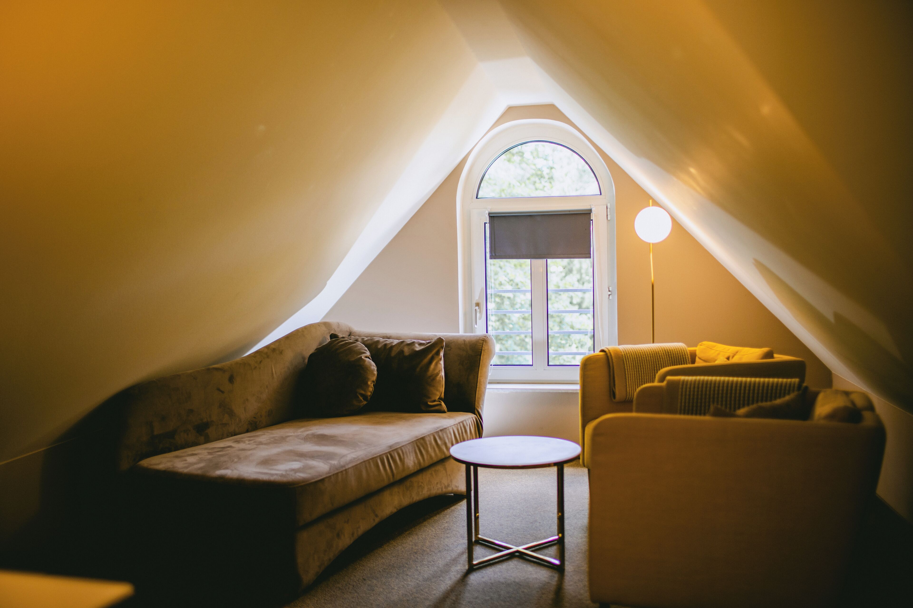 Acogedor dormitorio en ático con techo inclinado, un sofá, una silla y una pequeña mesa.