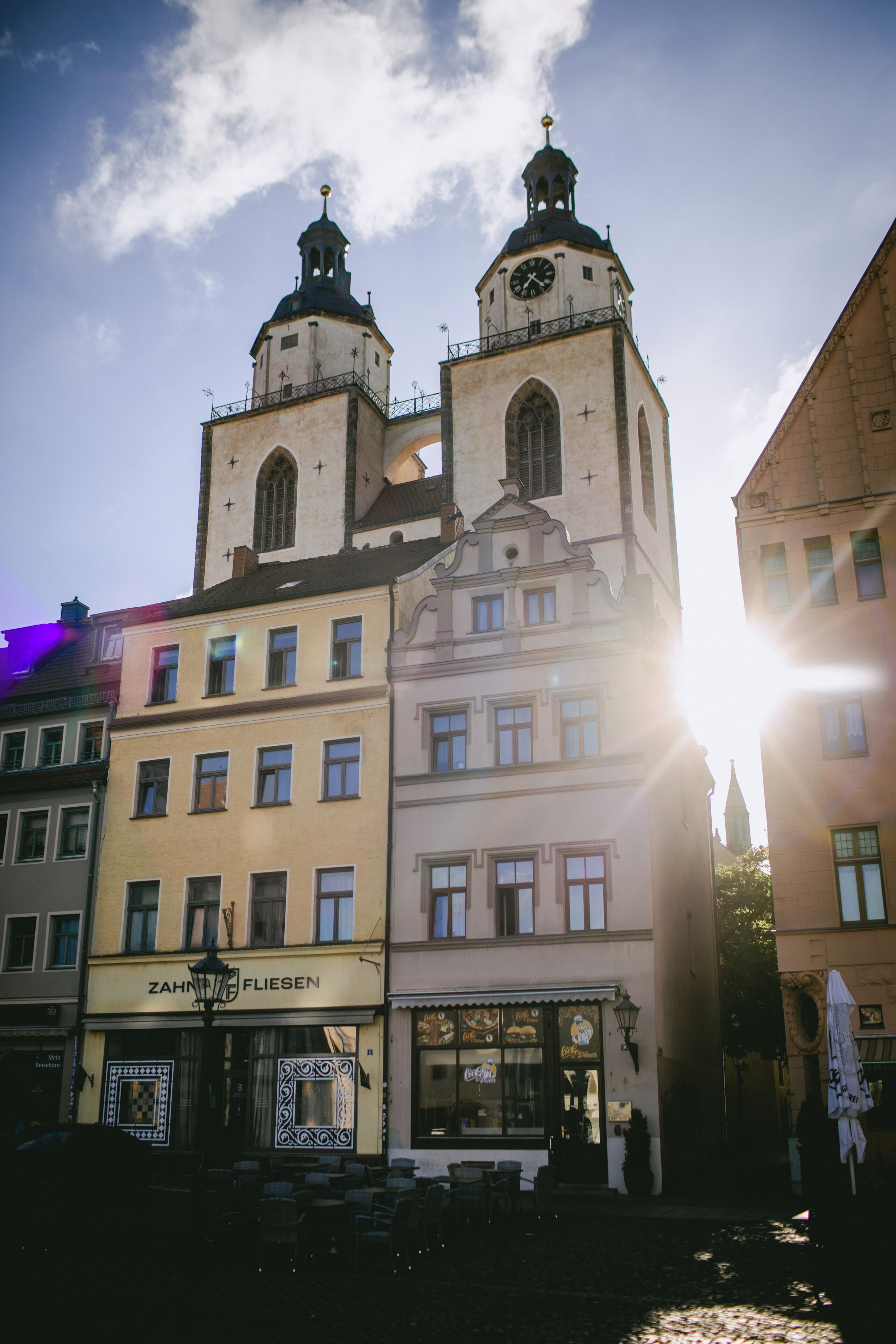 A historic building with two prominent towers, a clock, and a restaurant named 'ZAHN FLIESEN' at the ground level.