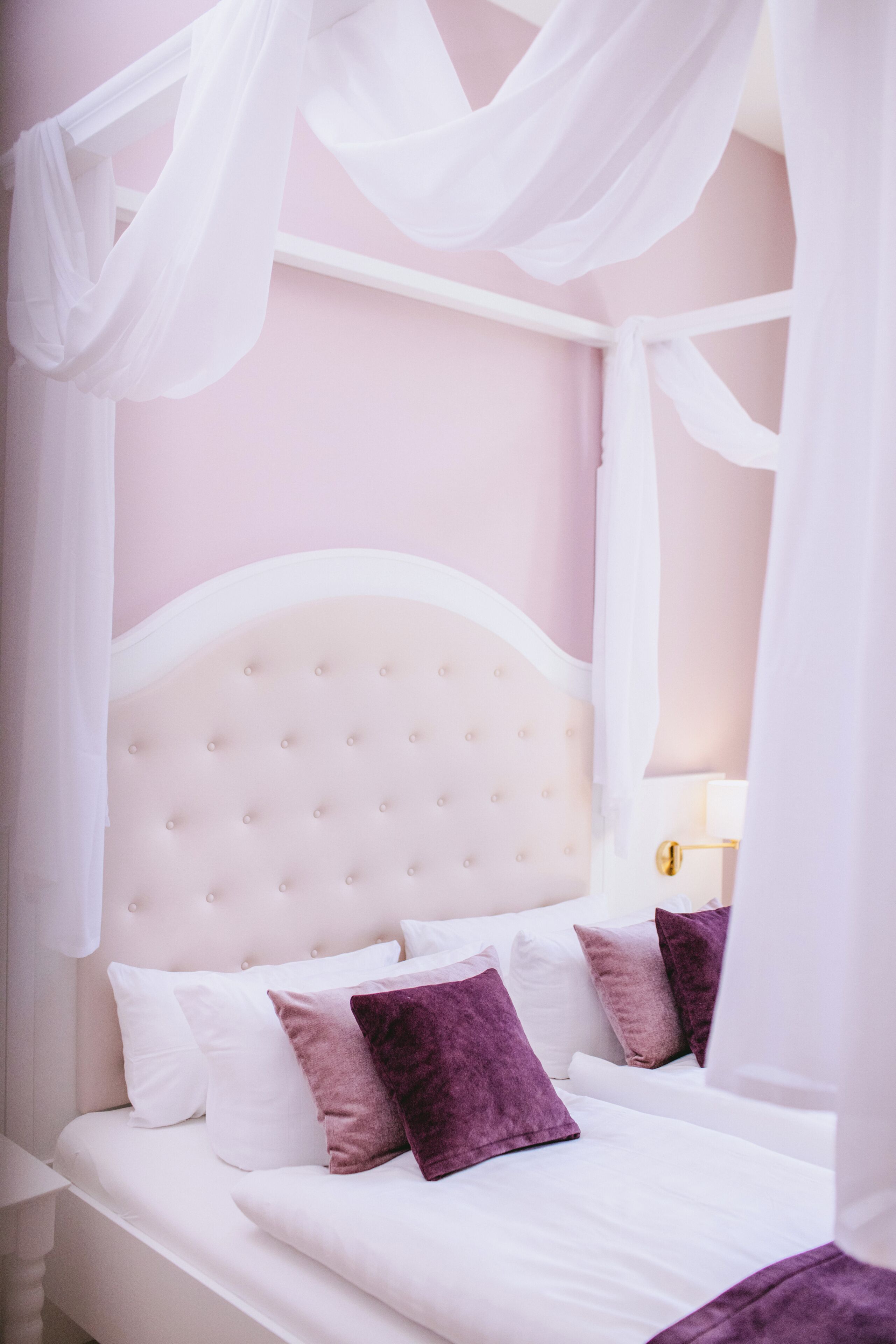 A bedroom with a canopy bed, white bedding, and a headboard with tufting.