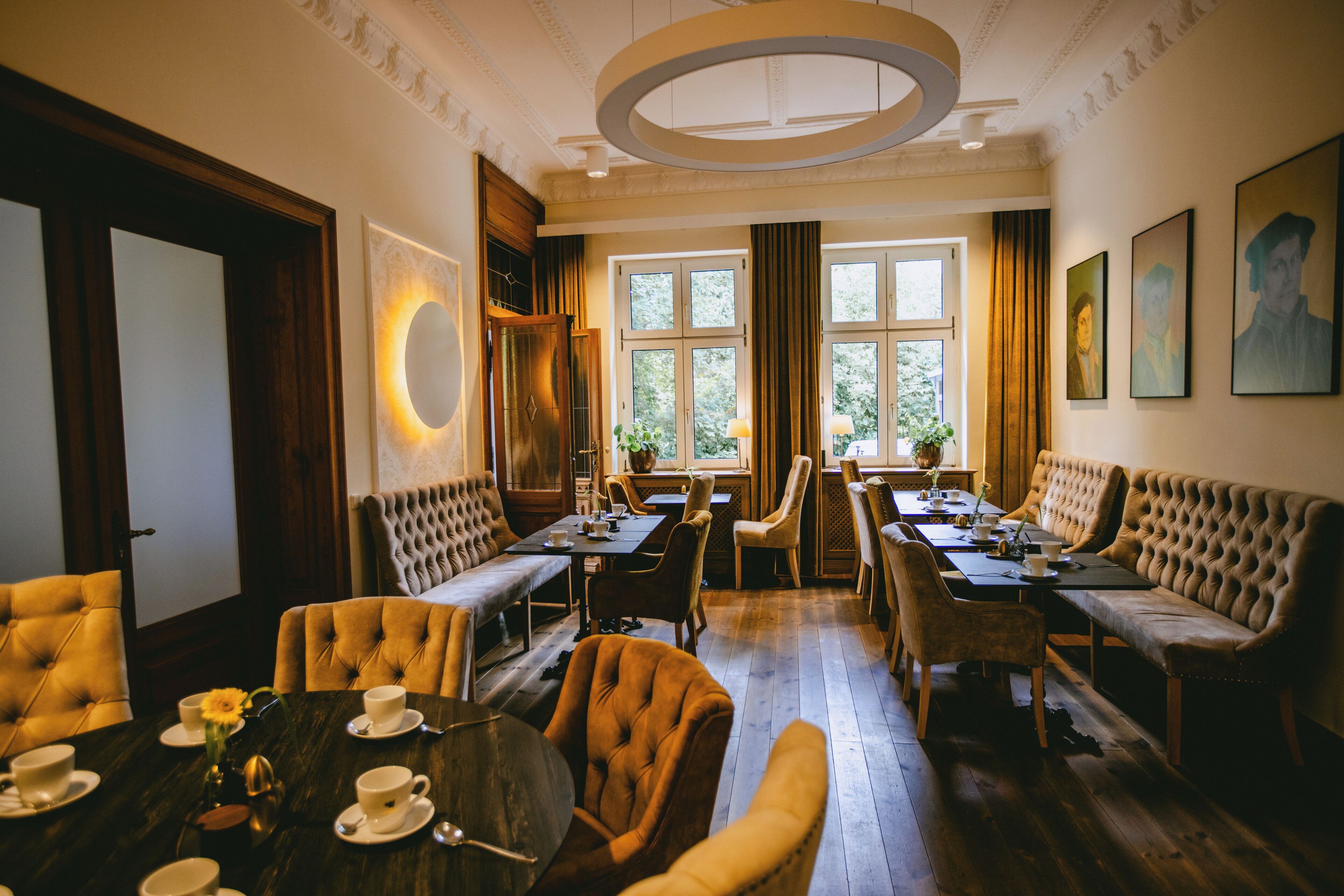 A room with a dining area featuring a long table and multiple chairs, a seating area with sofas and a bench, and a large window with curtains.
