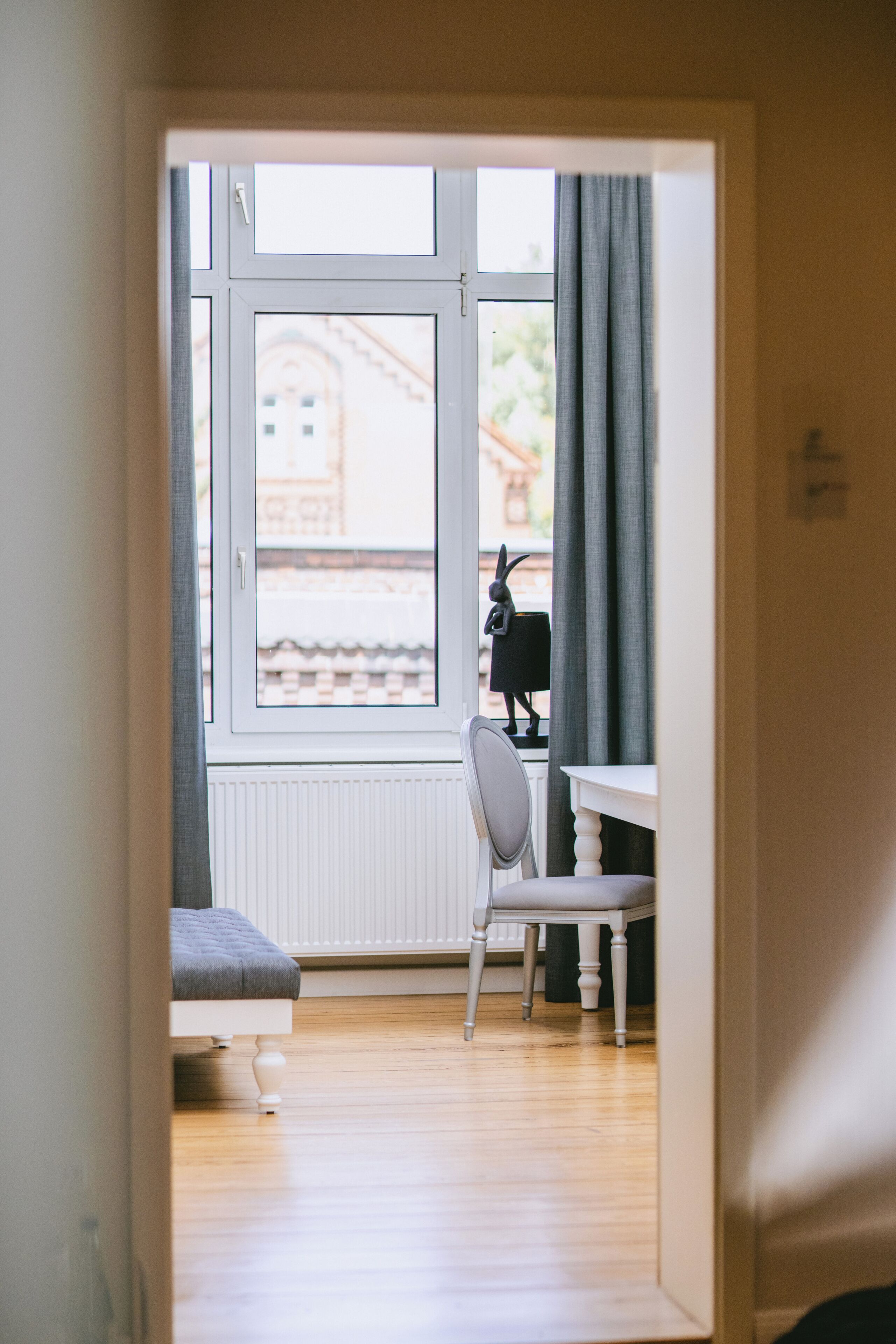 Ein Zimmer mit Bett, Stuhl, Tisch und Fenster mit Blick auf Gebäude.