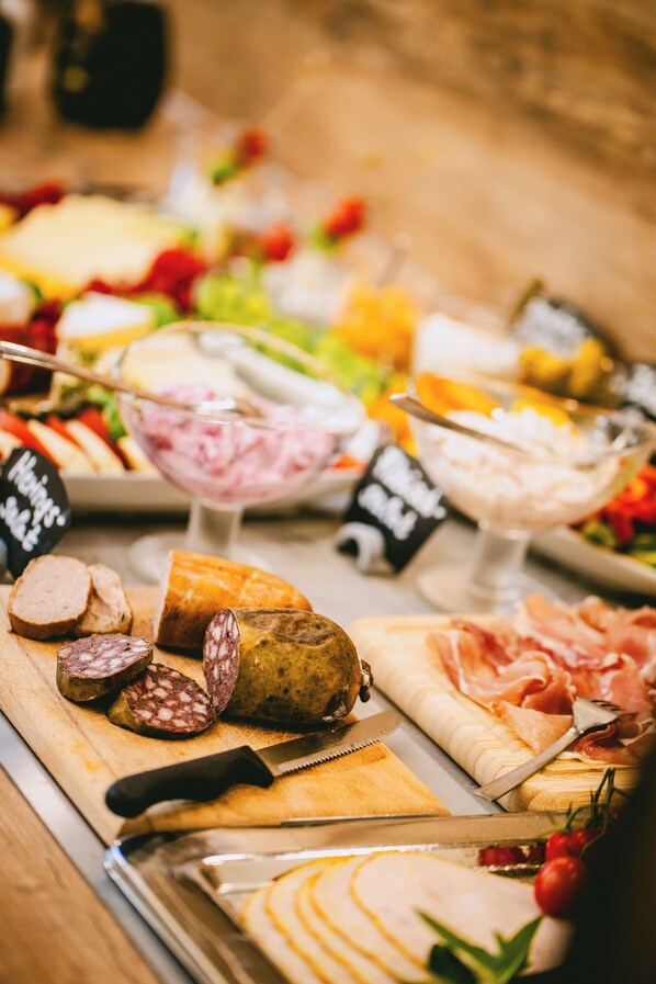 A variety of food items including sliced meats, cheeses, and vegetables on a wooden board. - Johanniter Hotel Wittenberg (Lutherstadt Wittenberg)