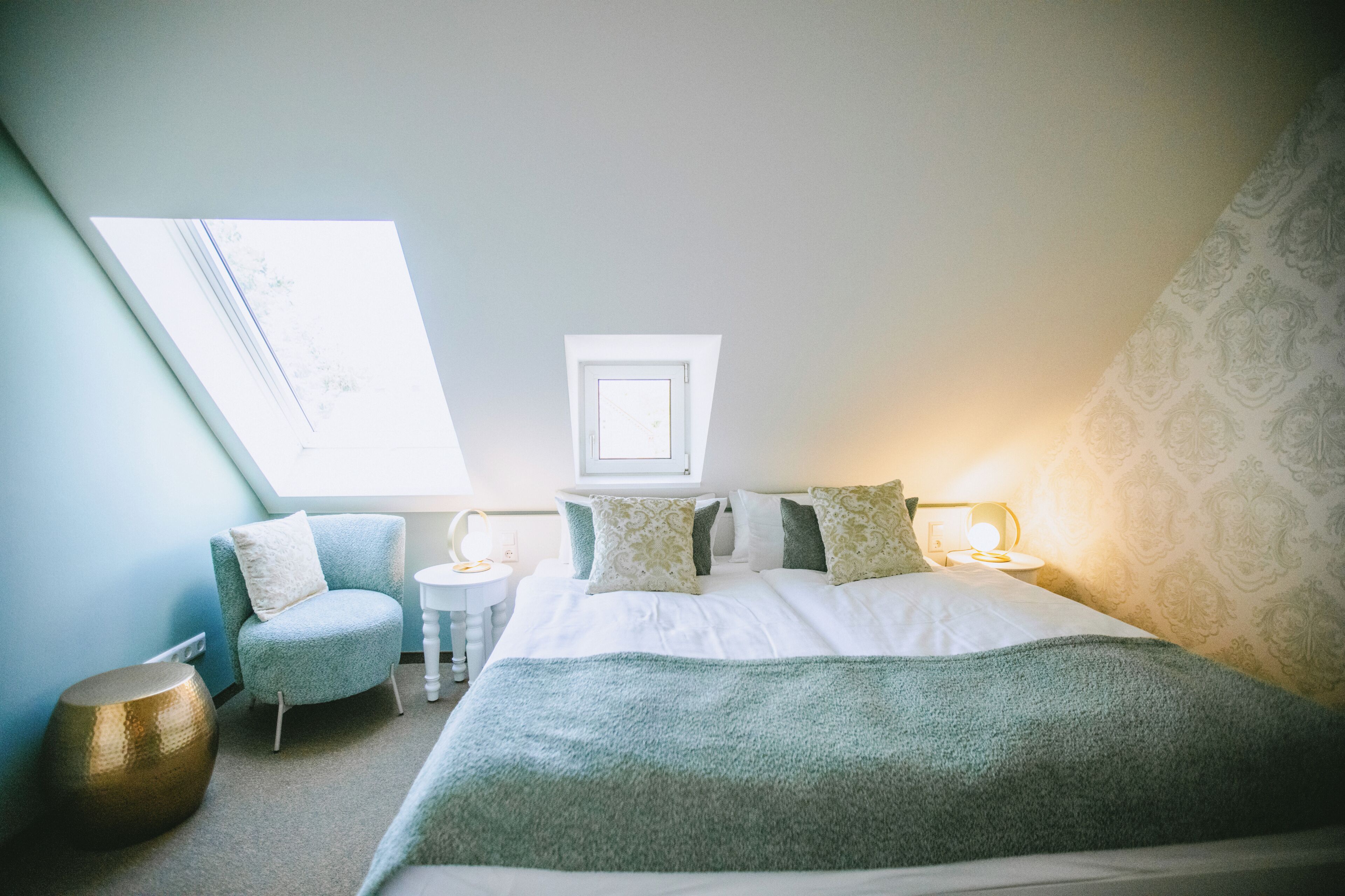 A bedroom with a large bed, a small round table, a chair, a mirror, and a window.