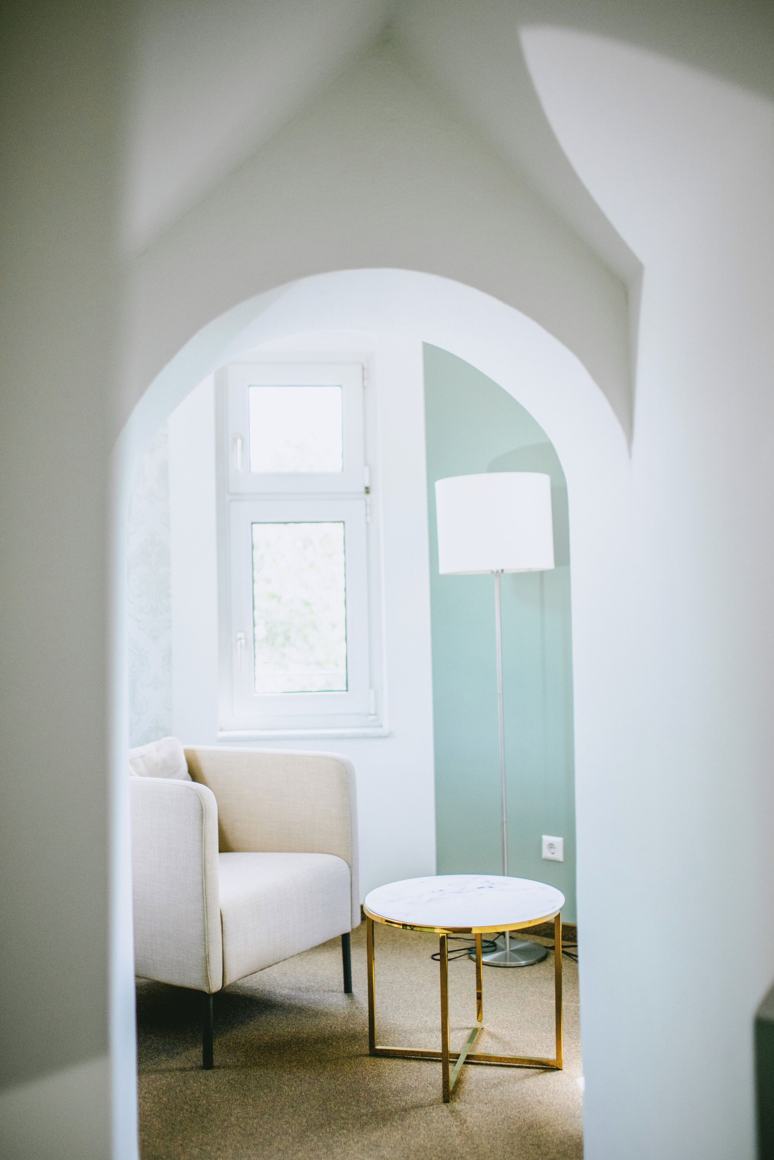 Una habitación con una silla blanca, una mesita redonda pequeña y una lámpara de pie.