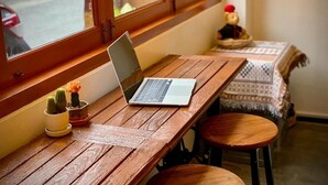 Une table en bois sur laquelle se trouvent un ordinateur portable, deux cactus en pot et une petite figurine.
