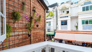 Un balcon avec un mur en briques, des plantes en pot et une vue sur les bâtiments voisins.