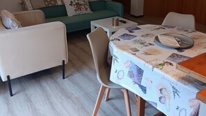 A living room with a green sofa, a white armchair, a dining table with a floral tablecloth, and a wooden cabinet. - ‘Tosca 5 L.T.I.’ Apartment with Balcony and Air Conditioning (Pisa)
