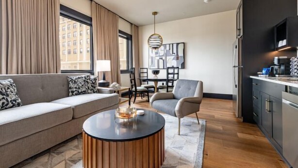 A modern living room with a sofa, a round coffee table, and a dining area with chairs and a table. - 1BR Penthouse Steps to French Quarter The Mayfair (New Orleans)