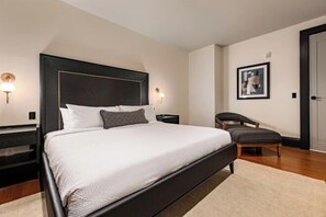 A bedroom with a large bed, bedside tables, a chair, and a framed picture on the wall. - 1BR Penthouse Steps to French Quarter The Mayfair (New Orleans)