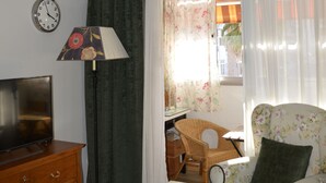 A living room with a television, a lamp, a table with a remote control, and a window with curtains. - Room in Sevilla (Santa Justa) (Sevilla)