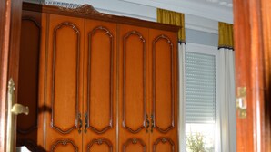 A bedroom with a wooden wardrobe, a bed with a floral bedspread, a red patterned rug, and a ceiling light fixture. - Room in Sevilla (Santa Justa) (Sevilla)
