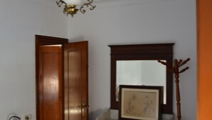 A bedroom with a wooden wardrobe, a bedside table, a mirror, and a ceiling light fixture. - Room in Sevilla (Santa Justa) (Sevilla)