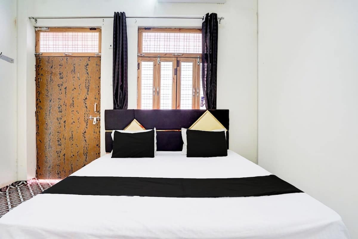 Une chambre d’hôtel avec un lit, deux fenêtres avec des rideaux, une porte ornée de motifs et un mur uni.