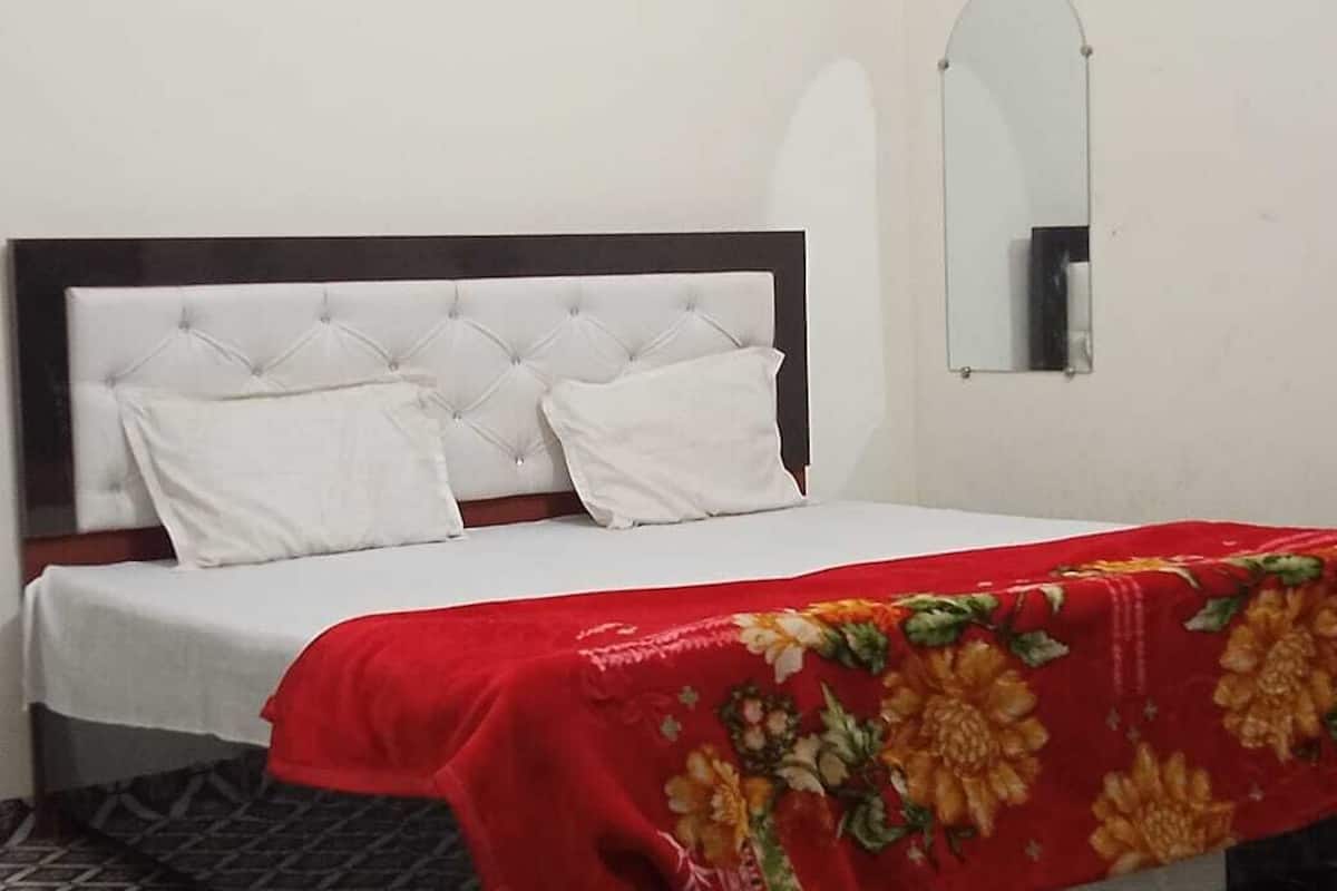 Un lit avec une tête de lit blanche, des oreillers blancs et une couvre-lit à motifs floraux rouges.