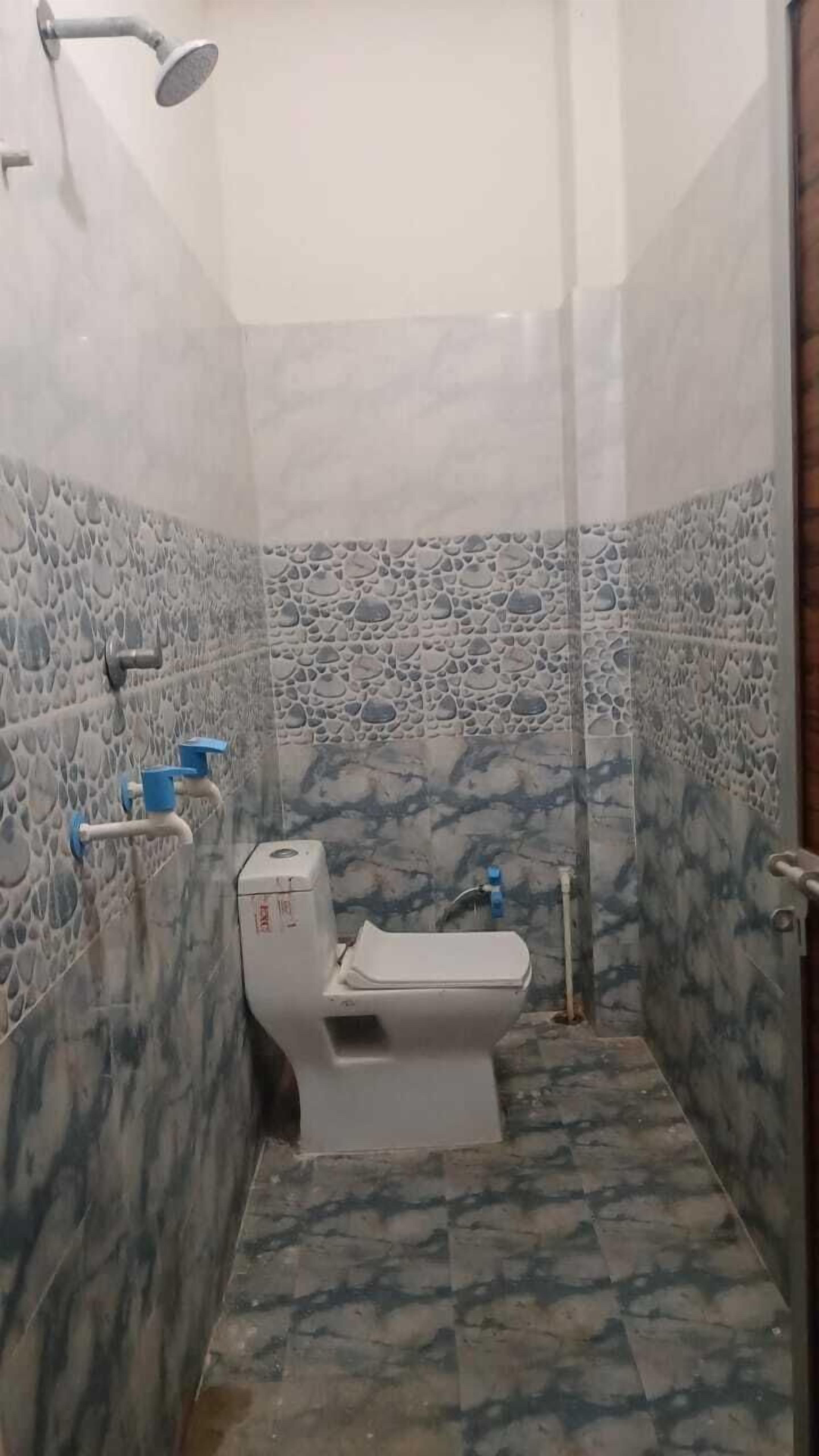 A small bathroom with a toilet, a blue faucet, and a showerhead.