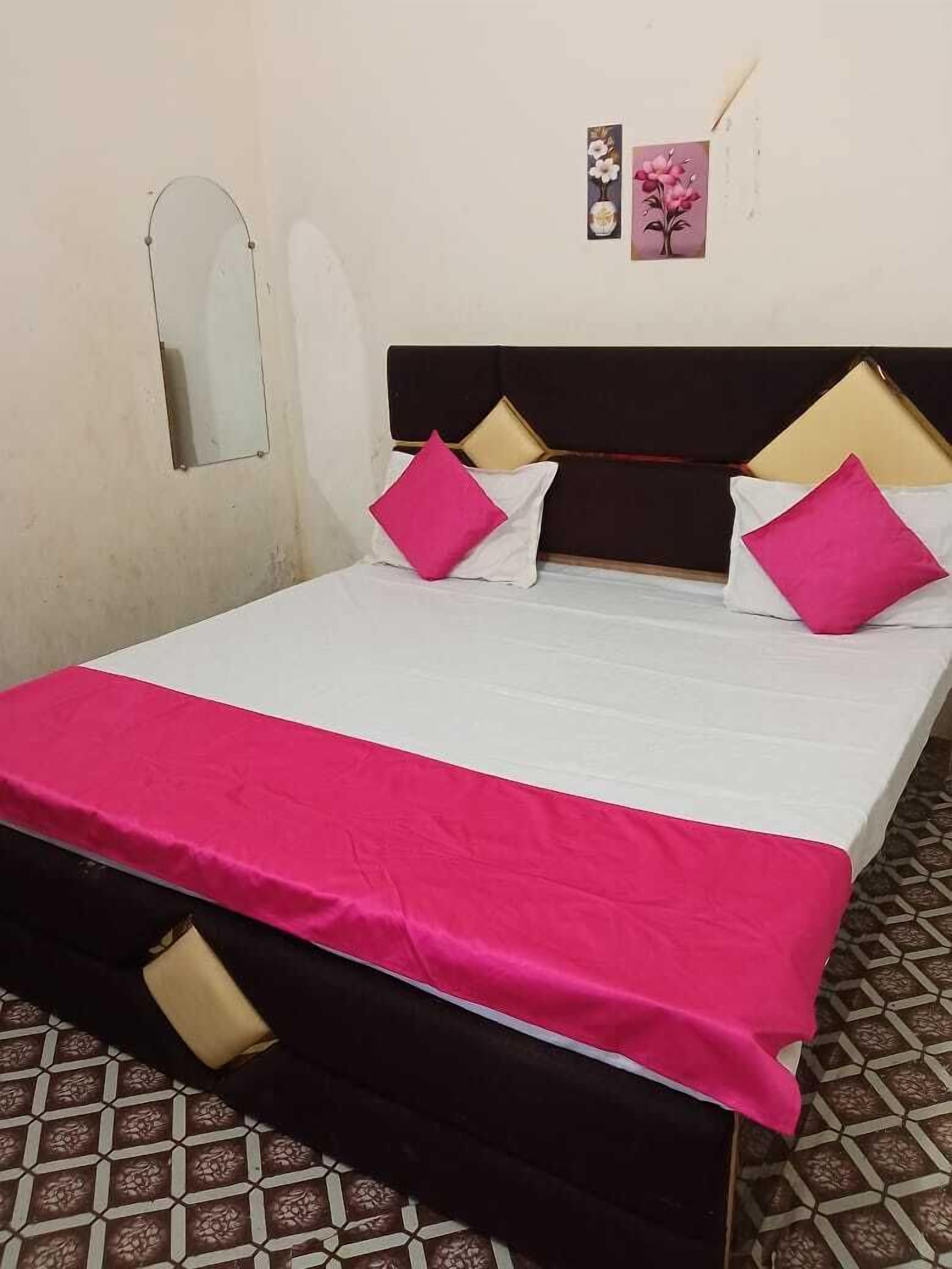 Ein Bett mit weißer und rosa Bettdecke, zwei rosafarbene Kissen und ein dunkles Kopfteil.
