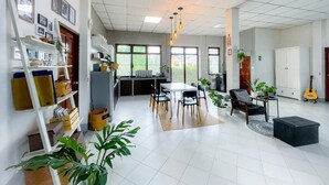 A spacious living area with a dining table, chairs, a sofa, and a coffee table. There are potted plants, a guitar, and a cabinet with items on the shelves. - Silpasom ARTstay Suratthani (Phunphin)