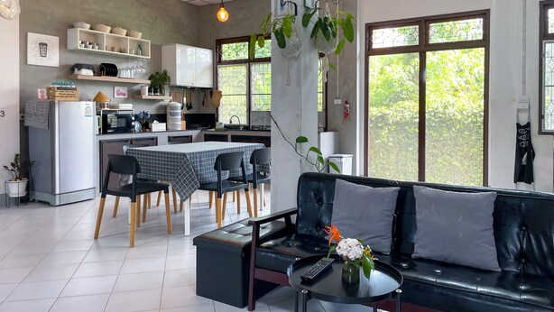 A modern kitchen with white cabinets, a refrigerator, and a dining area with a table and chairs. - Silpasom ARTstay Suratthani (Phunphin)