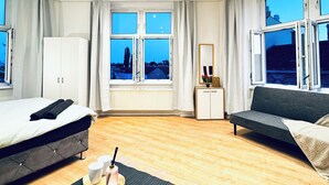 A modern hotel room with two beds, a sofa, a small table with a tray, and large windows offering a city view. - Cozy 4BR Apartment Near Kaufpark (Vienna)