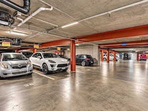 Eine mehrgeschossige Parkgarage mit Autos in markierten Stellplätzen, Betonpfeilern und darüberliegenden Leitungen.