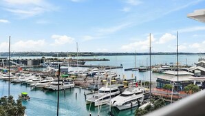 A marina with multiple boats docked, a large building with a curved roof, and a clear view of the water and distant land. - Modern Harbourside 1BR w Balcony Zodiak Stays (Auckland City)