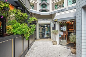 Ein Hotelgang mit hängenden Pflanzen, einem Schild mit der Aufschrift 'The Sebel Auckland' und einer Giraffenskulptur vor einem Geschäft.