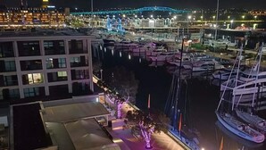 A marina with boats docked, a bridge in the background, and a building with illuminated windows. - Modern Harbourside 1BR w Balcony Zodiak Stays (Auckland City)