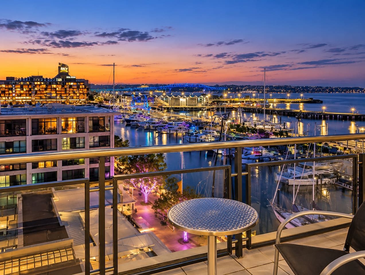 A marina with boats docked, a bridge in the background, and a building with a sign 'RACY'.