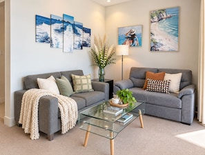 A living room with two grey sofas, a glass coffee table, and wall art depicting coastal scenes. - Central Auckland 1BR w/ Harbour Views Zodiak Stays (Auckland City)