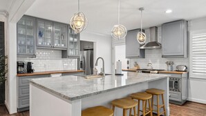 Eine moderne Küche mit einer großen Kochinsel, Holzbarhocker und Pendelleuchten.