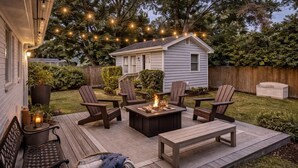 Eine Terrasse mit Gartenmöbeln, einem Feuerkorb und Lichterketten.