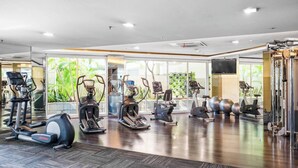 A gym with various cardio machines, mirrored walls, and a view of greenery outside. - Nahara by Kozystay - Kuningan (Jakarta)