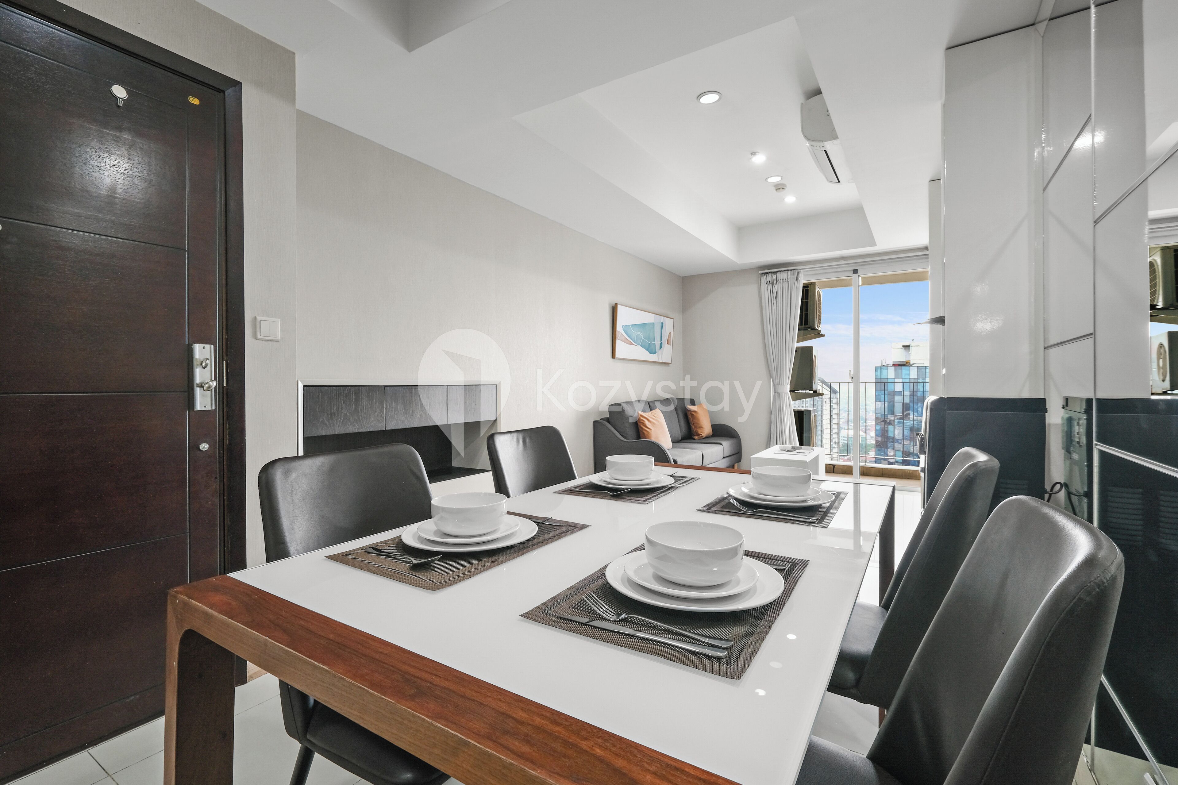 A modern dining area with a white table set for four, black chairs, and a dark wooden door.