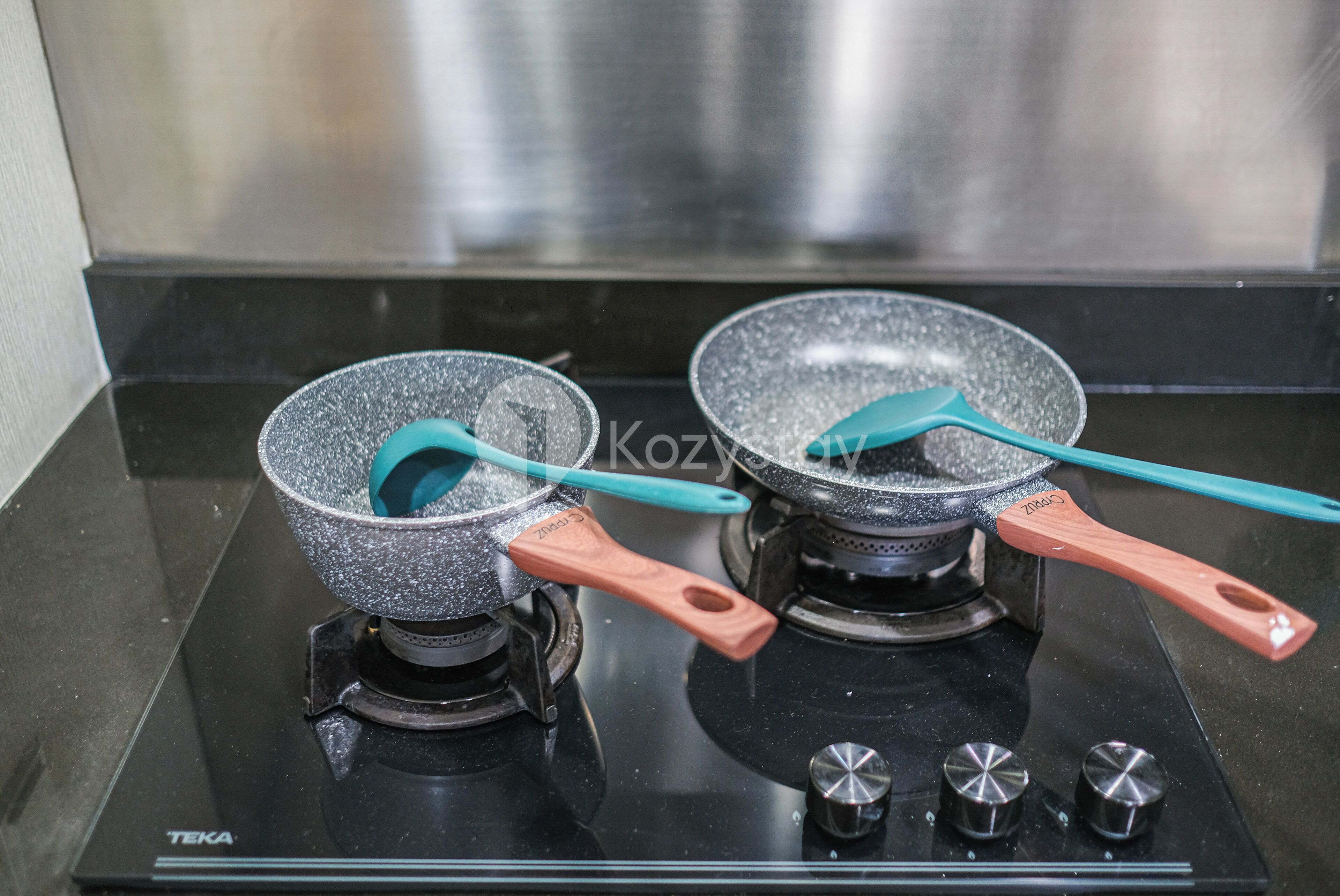 Two frying pans on a black stove with teal handles and a stainless steel range hood above.