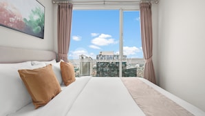 A hotel room with a large bed, two pillows, a view of the city through a window, and a painting on the wall. - Nahara by Kozystay - Kuningan (Jakarta)