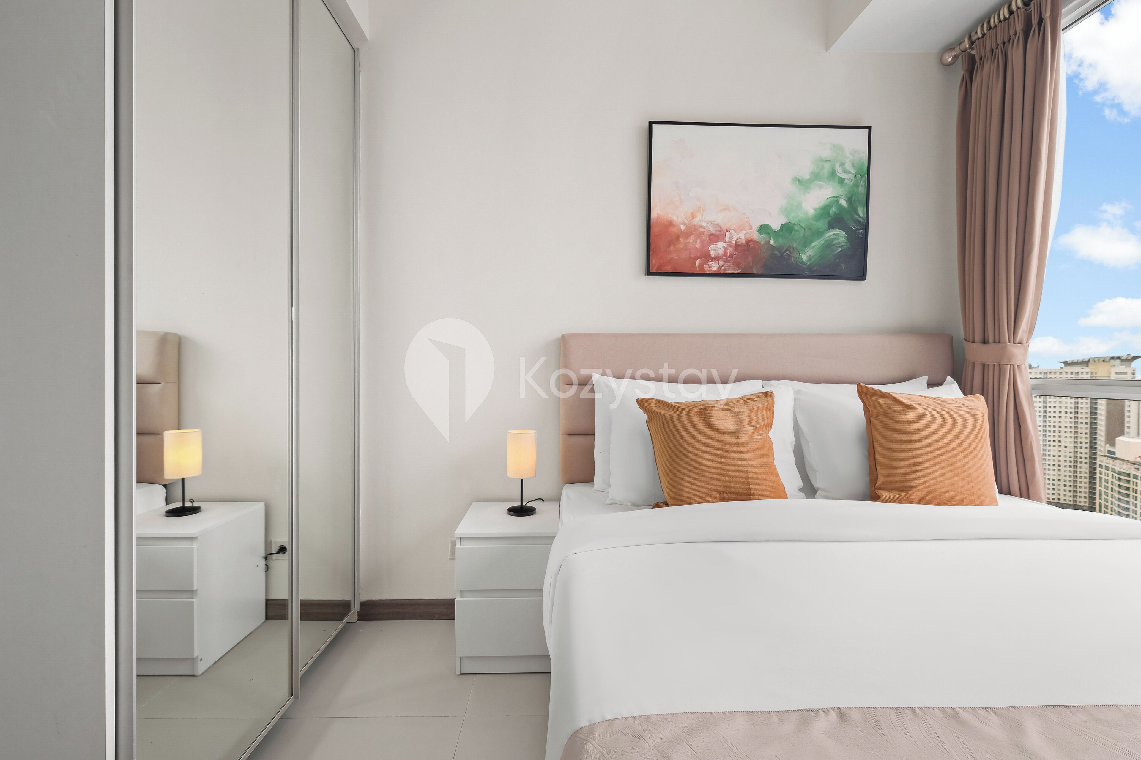 Een moderne hotelkamer met een groot bed, twee nachtkastjes met lampen, een grote spiegel en een lijst met een abstract schilderij aan de muur.