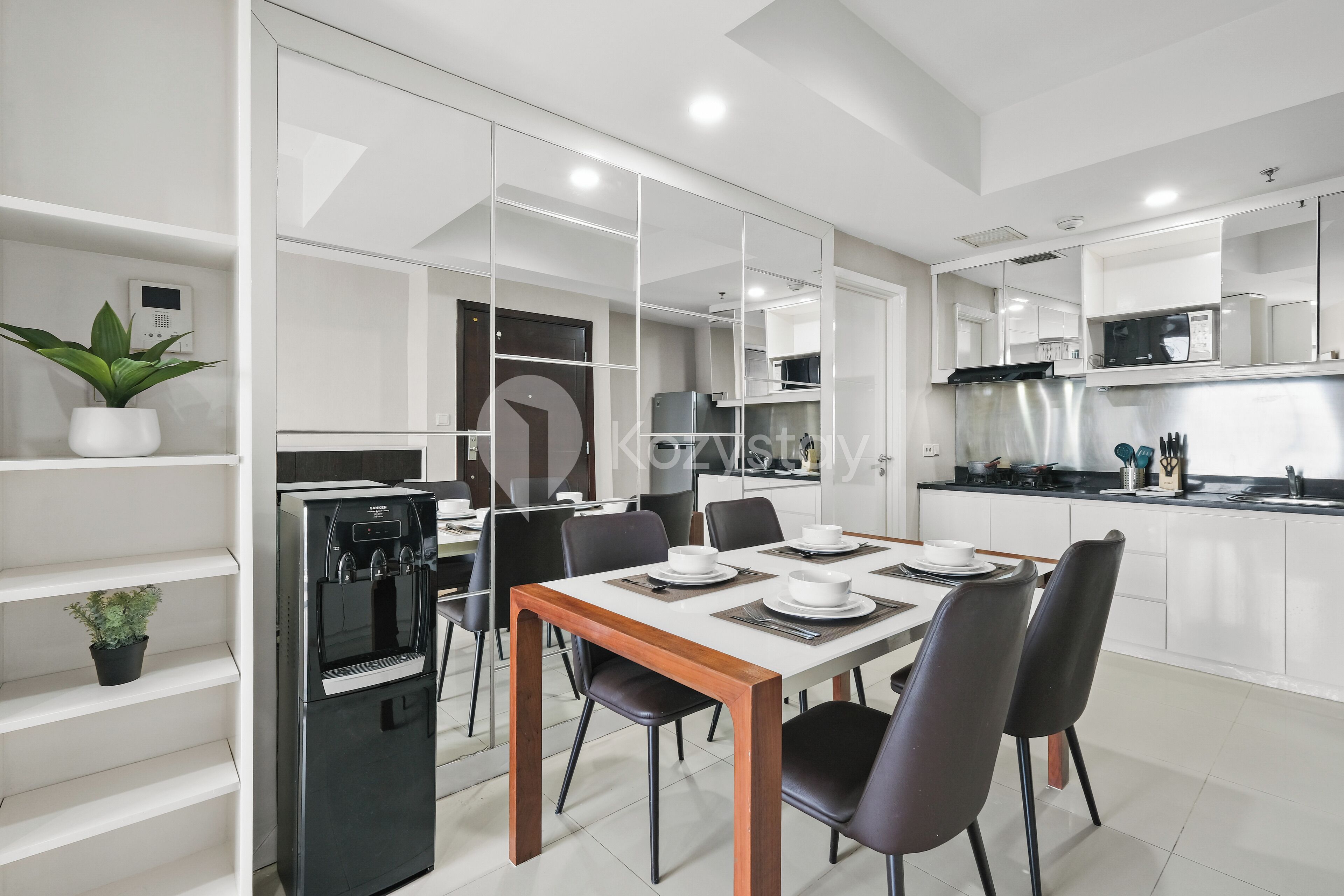 A modern kitchen with white cabinetry, a built-in oven, and a dining area with a wooden table and black chairs.