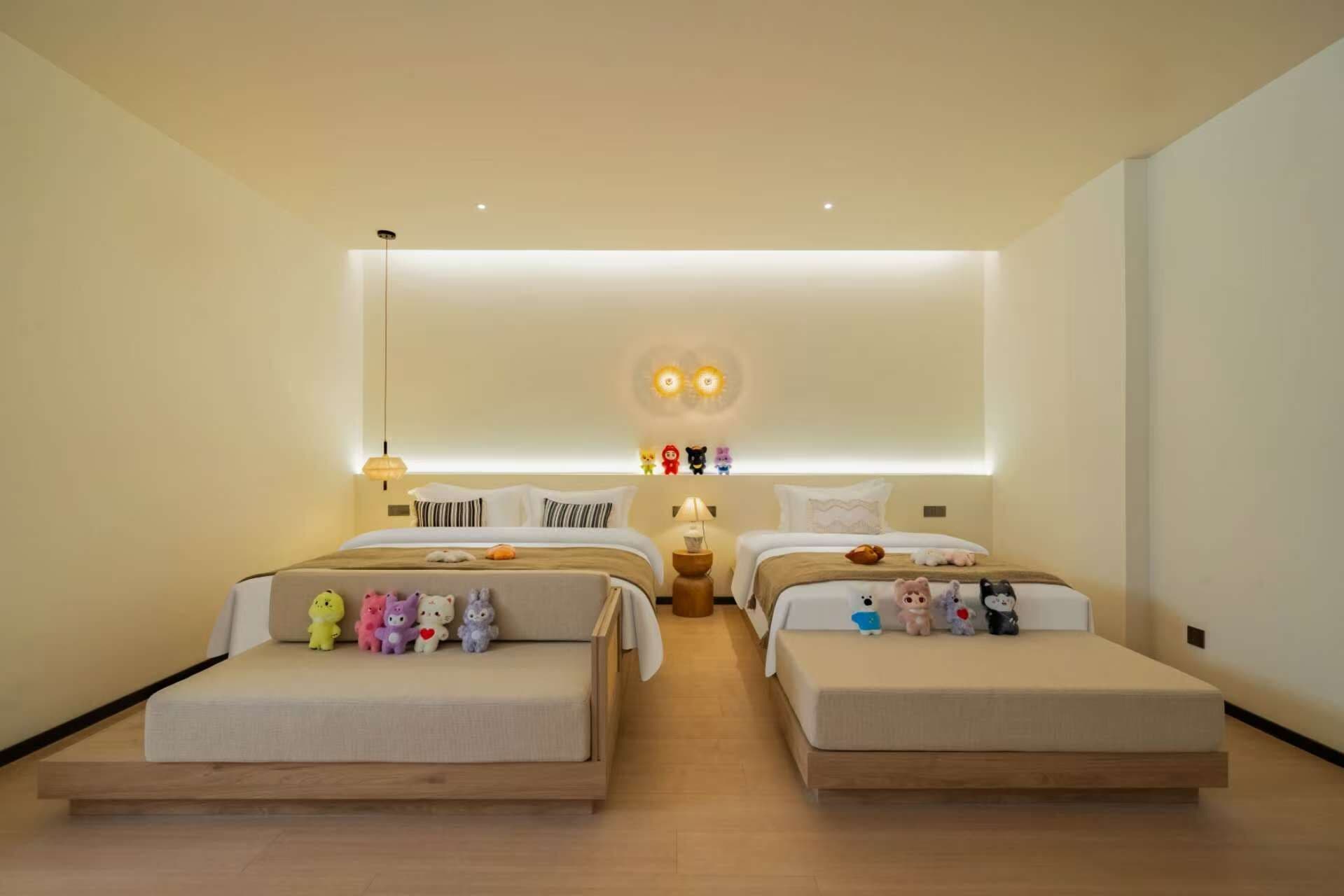 A modern hotel room with two beds, a central light fixture, and a small table with a lamp.
