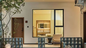 A modern entrance with a sliding glass door leading to a well-lit interior, a small outdoor seating area with a chair, and a decorative spherical object on the ground. - Yemuqingshan  (Ngawa Autonomous Prefecture)