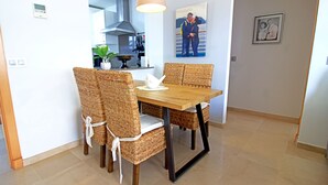 A dining area with a wooden table and wicker chairs, a modern kitchen in the background, and a framed picture on the wall. - Castillo Bajo in Torrox (Torrox)