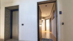 Pasillo de hotel con una puerta que da a una habitación, un felpudo y un panel de control en la pared.