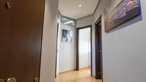 Un pasillo con piso de madera, una puerta a la izquierda y un cuadro enmarcado en la pared derecha.