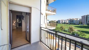 Un balcón con vistas a un barrio residencial, una puerta que da a un espacio interior y una barandilla.