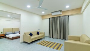 A modern hotel room with a bed, two sofas, a small table, and a ceiling fan. - Tribe Moro Balewadi  (Paud)