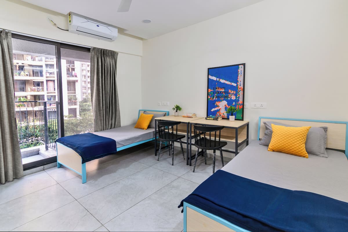 A hotel room with two beds, a desk, and a view of a residential area.