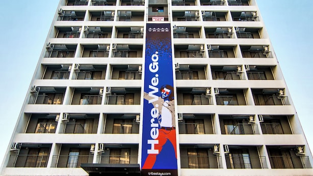 A high-rise hotel with multiple floors, large windows, and a prominent banner advertising a brand. - Tribe Moro Balewadi  (Paud)