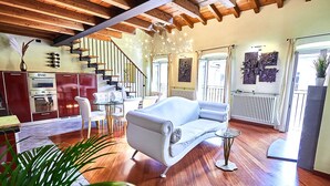 A spacious living area with a white sofa, wooden flooring, a staircase, and a kitchen in the background. - Atlas Apartments  (Bergamo)